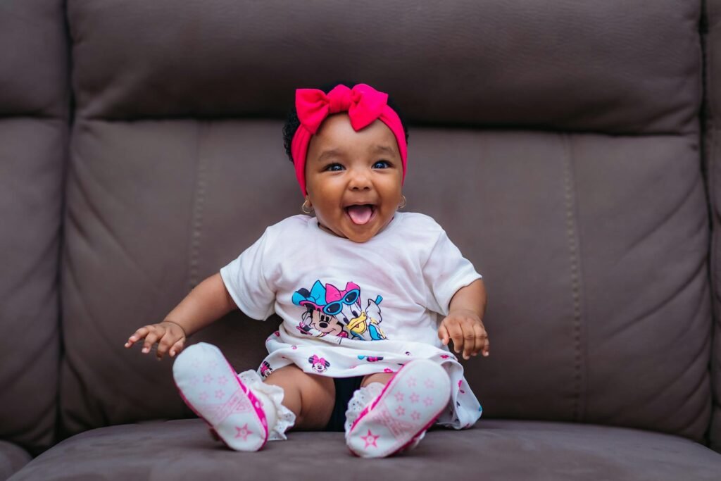 Cute baby with pink headband smiling joyfully on a sofa.