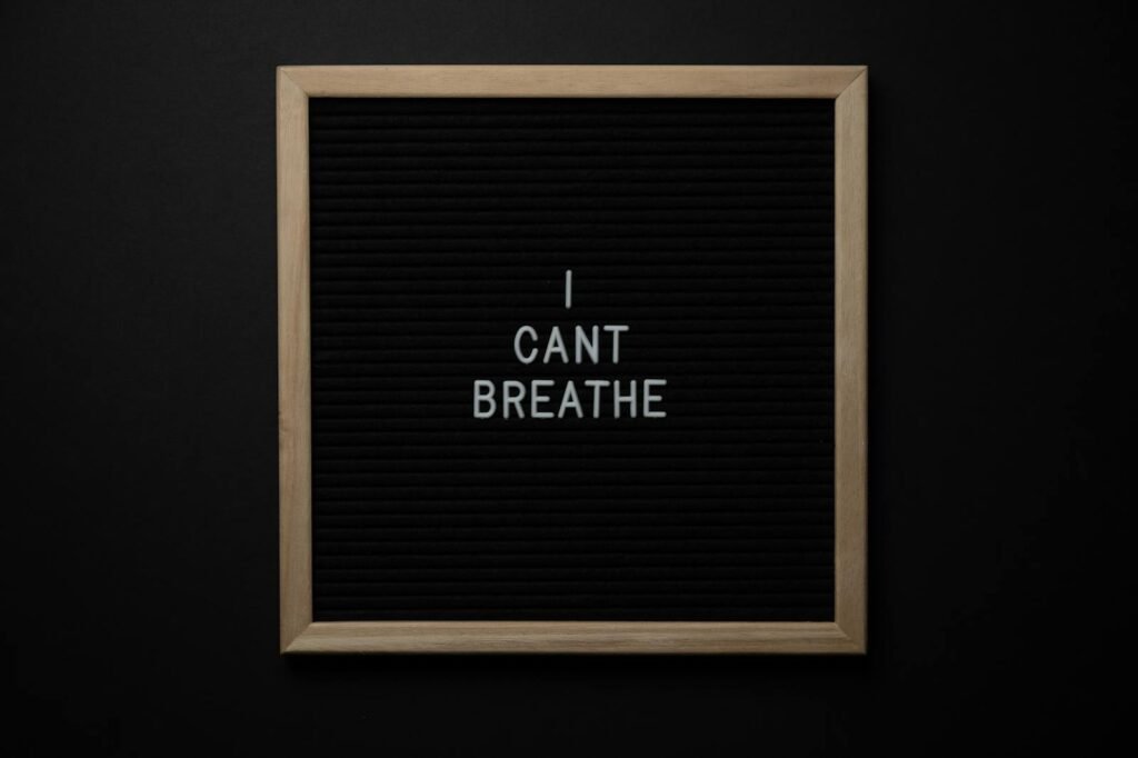 Top view of phrase I Cant Breath on small black signboard with light beige thin frame on black background