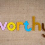 The word 'worthy' in colorful felt letters on a burlap texture, conveying positivity and value.